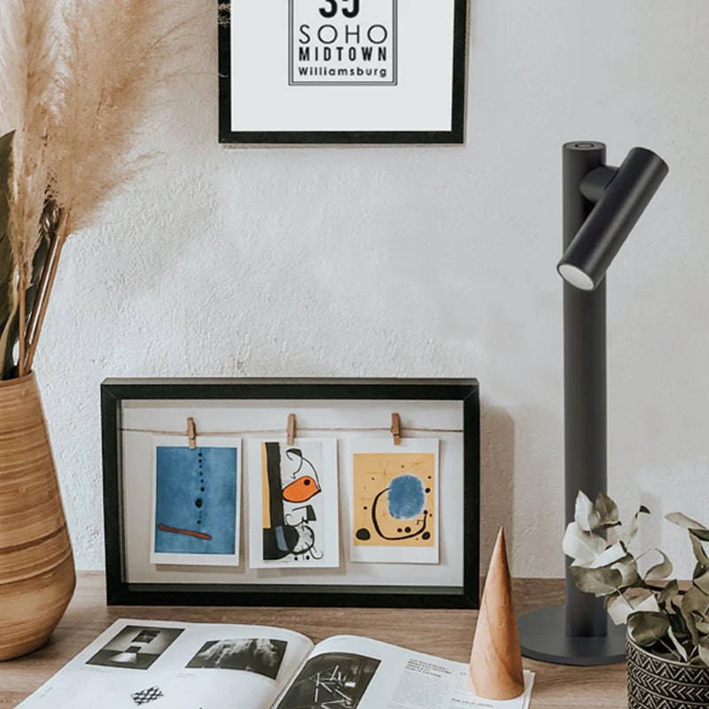 SPAZIO Zoom Rechargeable Table Lamp – dark lamp on a desk beside framed pictures