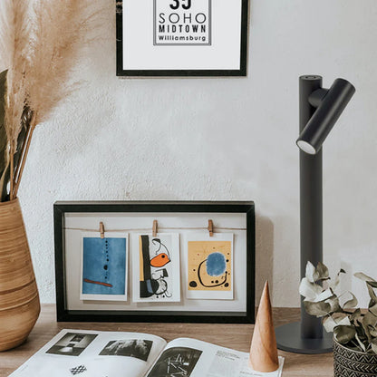 SPAZIO Zoom Rechargeable Table Lamp – dark lamp on a desk beside framed pictures
