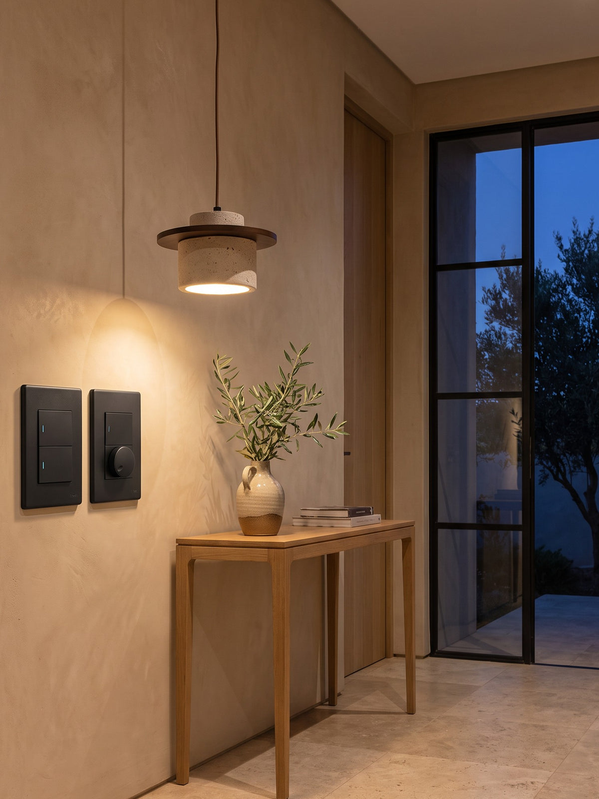 Synerji DECO matt black light switch and dimmer in an entrance hall at dusk, under a SPAZIO Seattle pendant